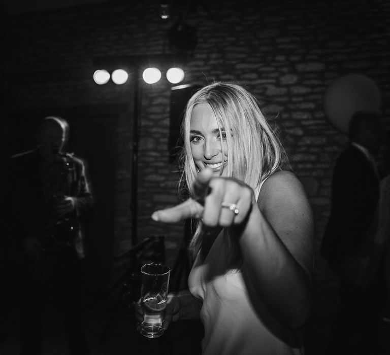 Bride in white Charlie Brear wedding dress points at the camera during evening party at Caswell House wedding