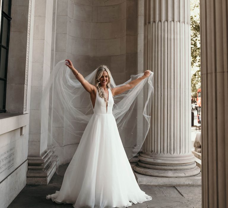 Bride throws back veil under white pillars