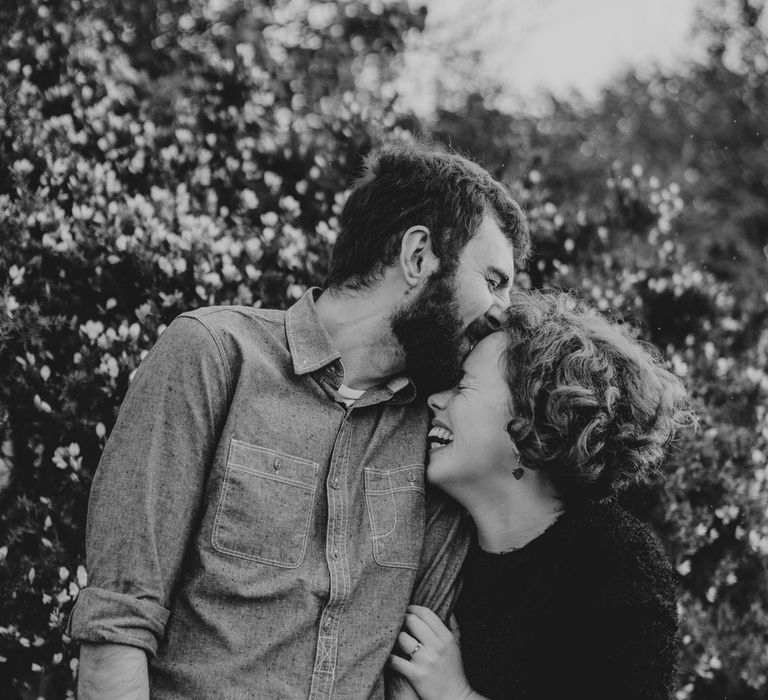 Man kisses his fiancé on the head in black & white image