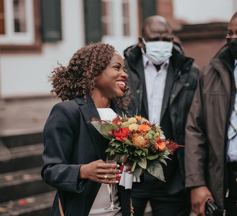 Bride wears jacket outdoors carrying Autumnal bouquet