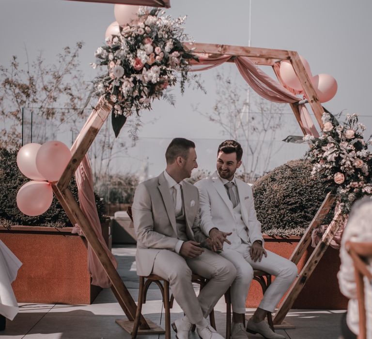 Grooms under geometric wedding arch at rooftop wedding