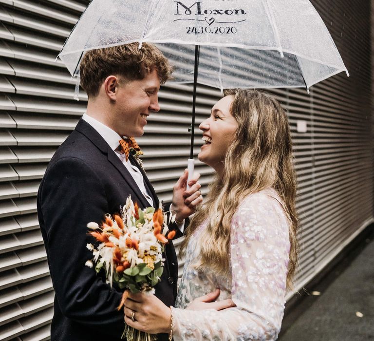 Bride and groom holding each other under umbrella 