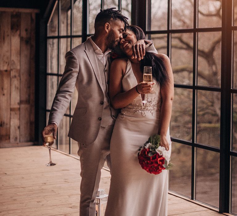 Bride & groom laugh as bride holds glass of champagne and floral bouquet 