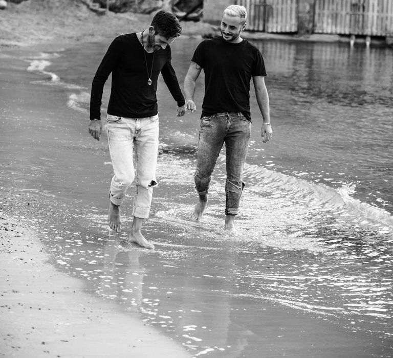 Black & white image of grooms walking along the sand