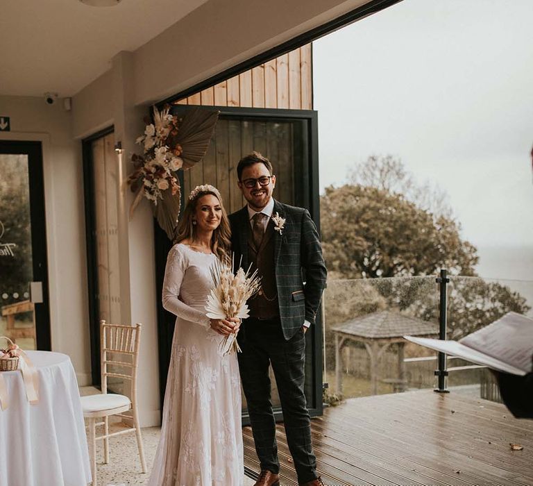 Bride and groom exchanging vows at their autumn seaside elopement with dried flower arrangement and bouquet 