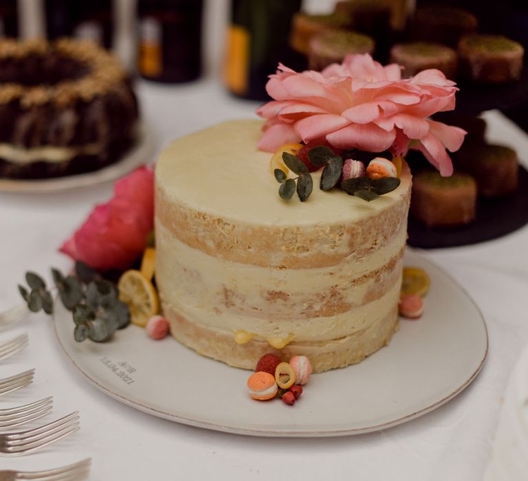 Triple layer sponge naked wedding cake with pale yellow icing and dried fruit, foliage and floral decor at garden party wedding in Devon