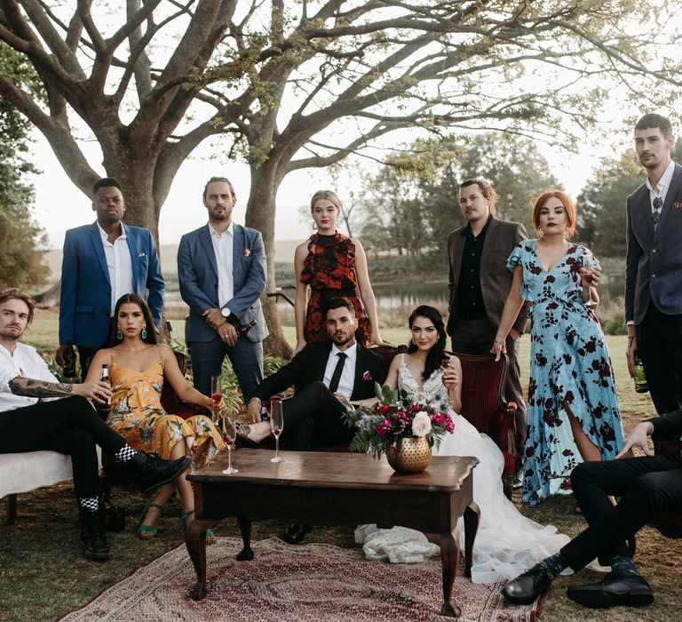 The bride and groom with their wedding party, sat outside with antique furniture and rugs