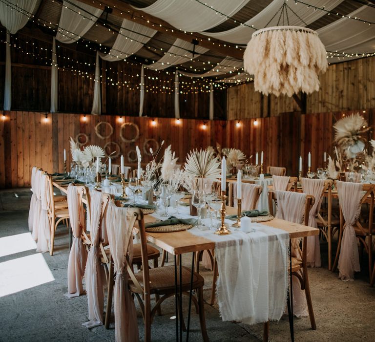 Bohemian styled wedding reception t East Yorkshire Barns with fairy lights, pampas grass chandelier and hoop decor, wicker place mats and pink chiffon chair back covers 