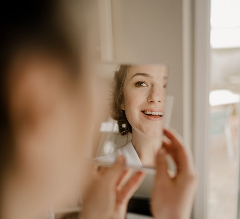 Bride smiles into handheld mirror before Dunluce Castle wedding