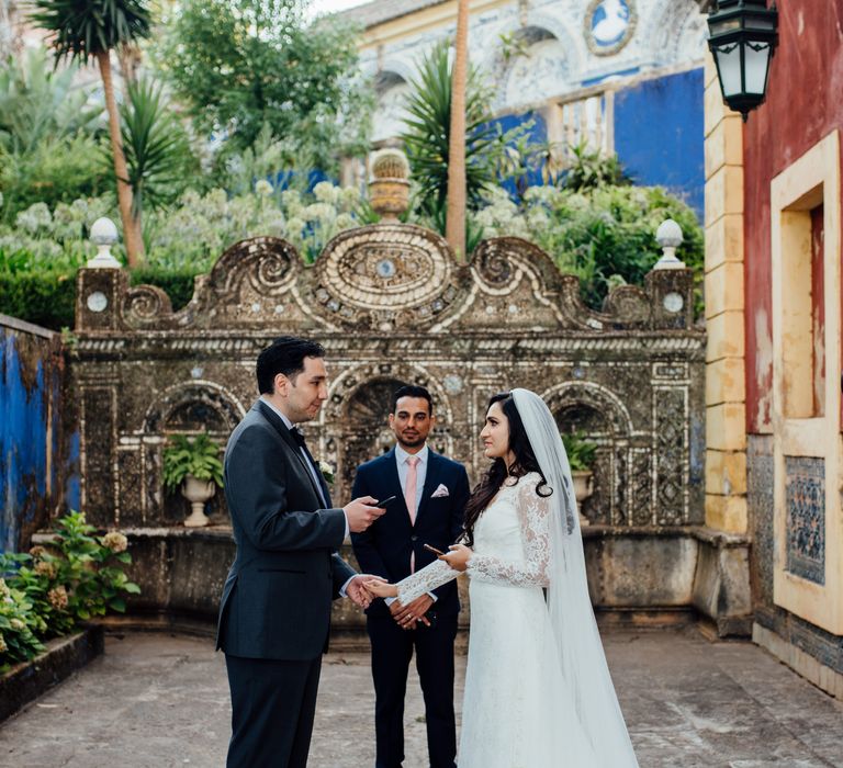 Bride & groom hold hands and look lovingly at one another during wedding ceremony outdoors