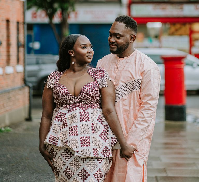 Black bride & groom wear traditional Senegalese outfits in colourful prints whilst looking lovingly at one another on their wedding day