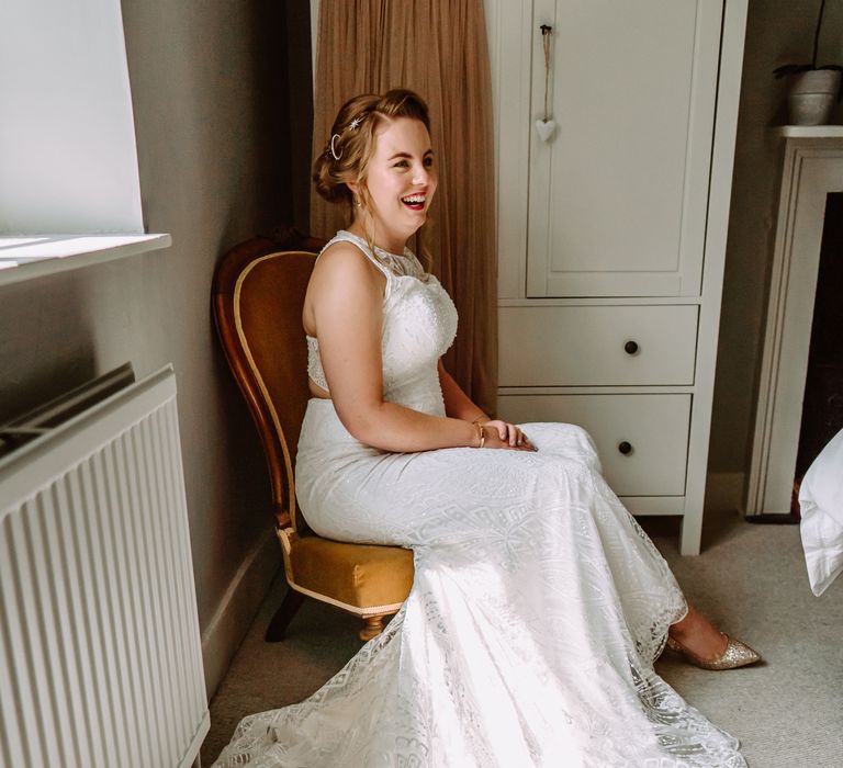 Bride laughs whilst wearing red lipstick and holding her hands in her lap on the morning of her wedding