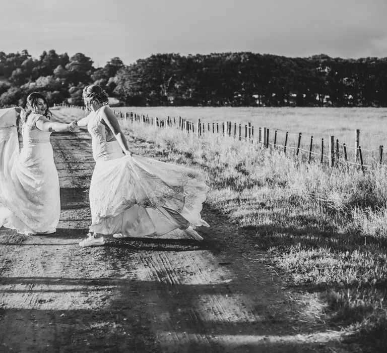 Brides hold hands and dance together through the countryside for Park Farm wedding