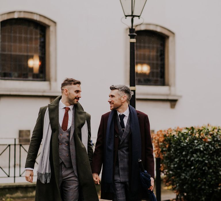 Grooms walk through London with one another as they looking lovingly toward each other 