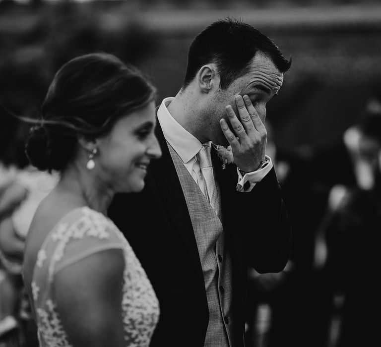 Groom wipes his eyes as he stands next to bride in Rime Arodaky wedding dress during outdoor wedding ceremony in Dorset 