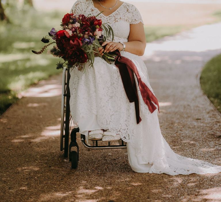 Beautiful Indian bride in a wheelchair wearing a lace wedding dress and holding a bright red, purple and pink wedding bouquet 