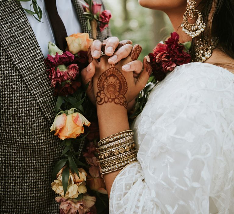 Close up of an Indian British bride and groom who are holding hands close to their chests.