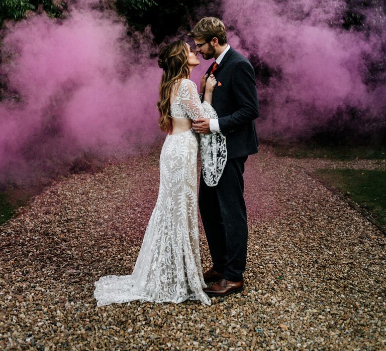 Boho, summer wedding at Preston Court with a purple smoke bomb portrait of a bride in a lace wedding dress and groom in a dark suit kissing