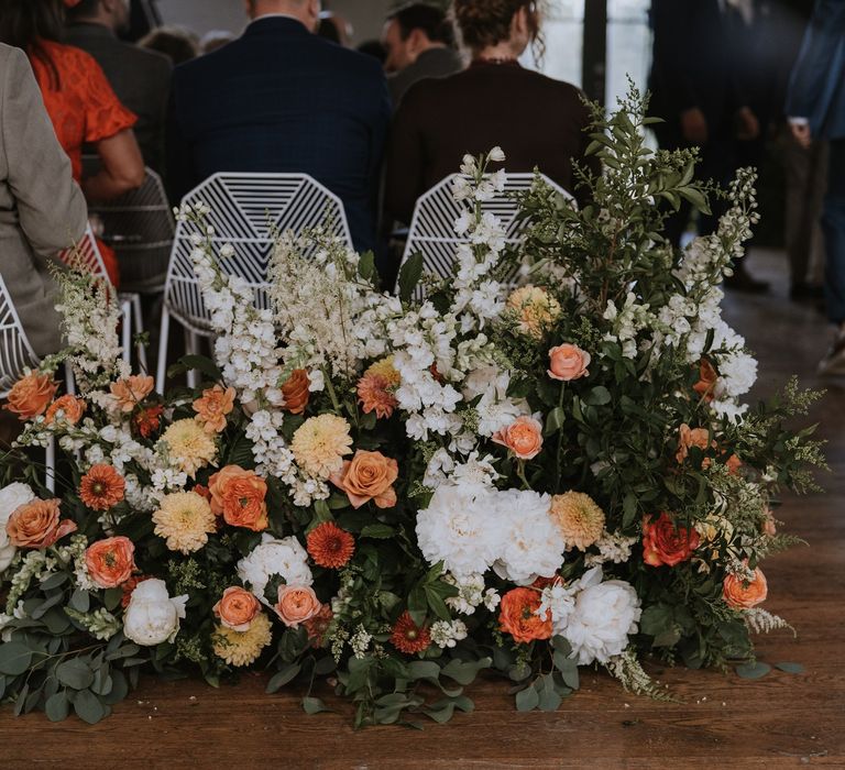 Geometric white metal ceremony chairs and white and peach wedding flowers