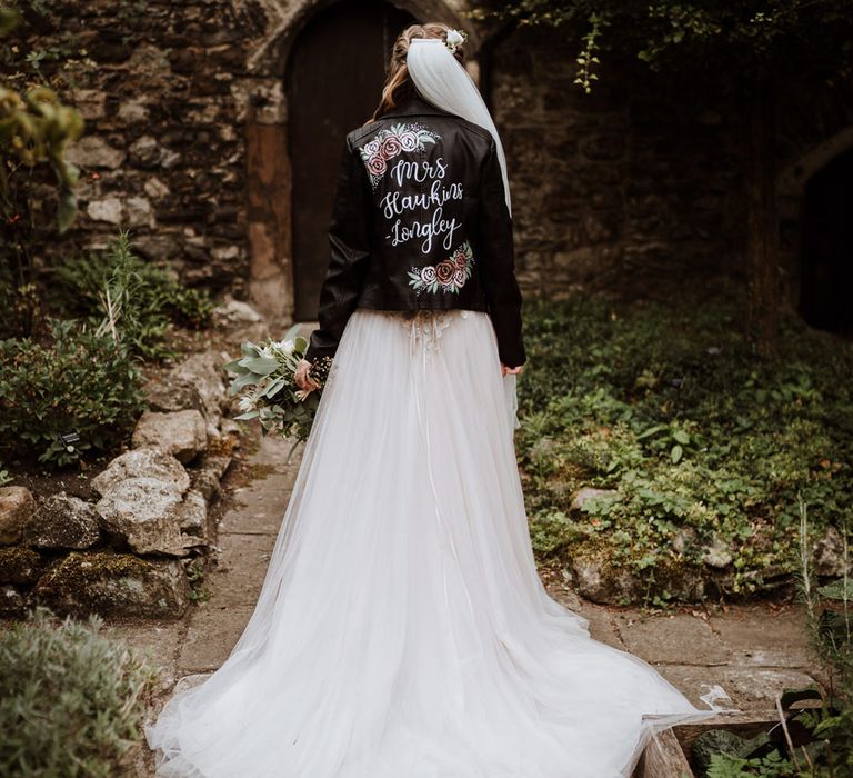 Bride in an A line wedding dress with puddle train in a customised leather jacket with rose design 