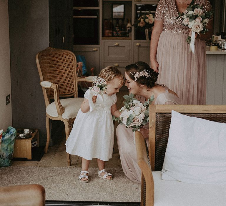 Bridesmaid in a pink chiffon dress kneeling down to talk to the flower girl in a white dress