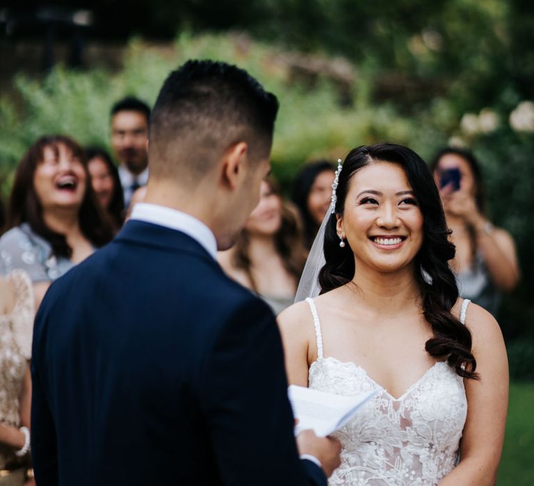 South Asian bride with long wavy hair smiles in an embellished wedding dress during the outdoor wedding ceremony 