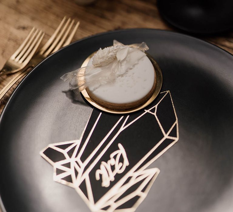 Place setting with black tableware, biscuit favour and geometric name place card 