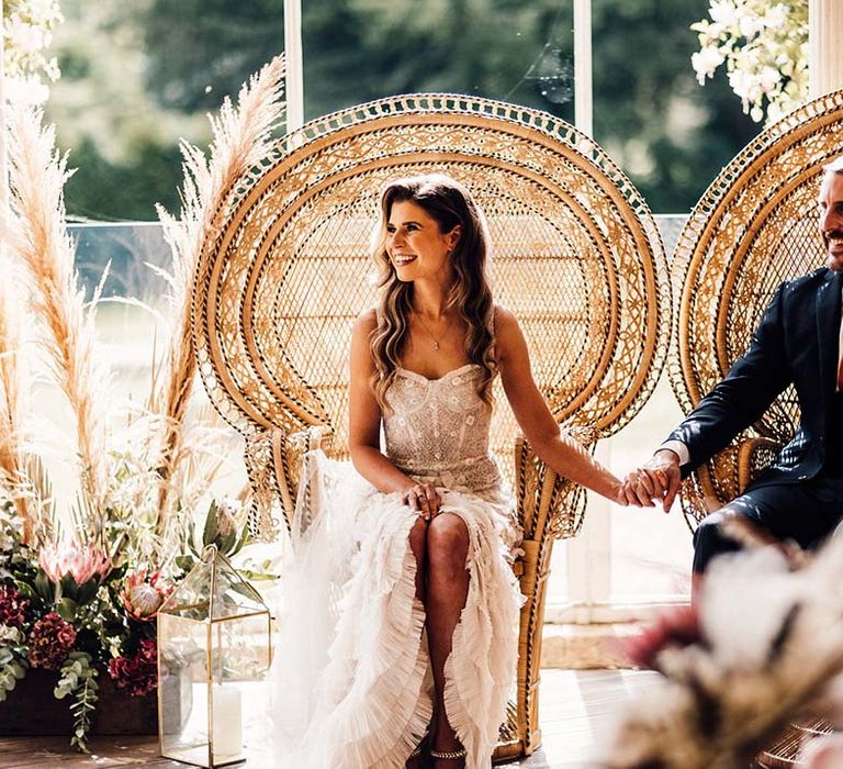 Bride & groom sit on peacock chairs on their wedding day