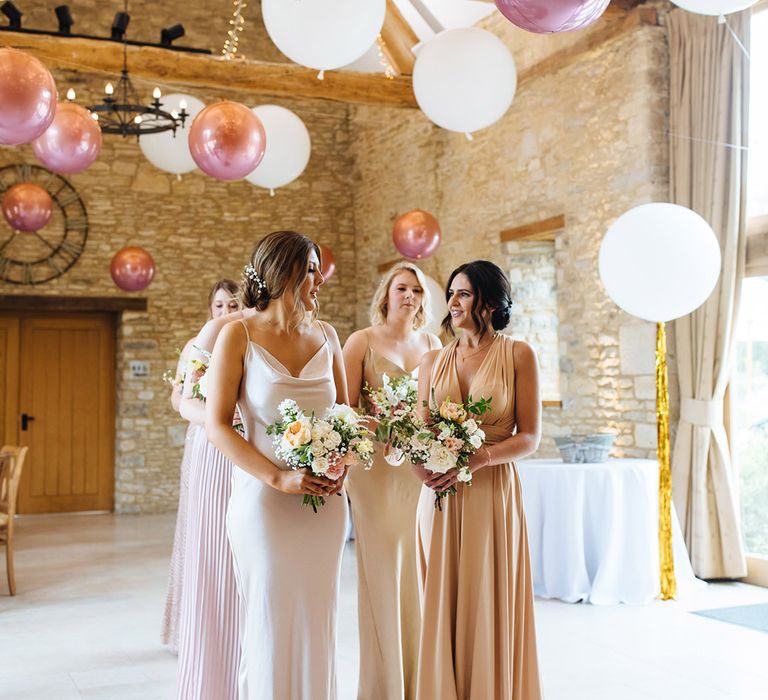 Bridesmaids in different pink dresses standing in Caswell House rustic barn wedding venue decorated with giant pink balloons an tassels 