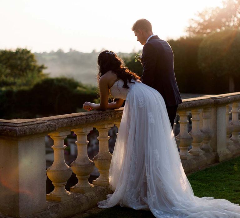 Bride leans across wall as the sun begins to set on her wedding day