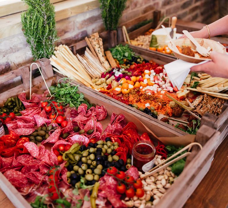 Mixed grazing boxes on wooden trays with charcuterie, cheeses and assorted snacks for festival inspired barn wedding