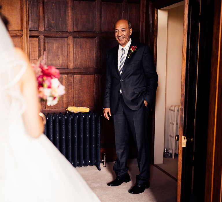 Man in dark blue suit with floral buttonhole and blue and white striped tie gets first look at bride in wedding dress with tulle skirt and veil before Elmore Court wedding