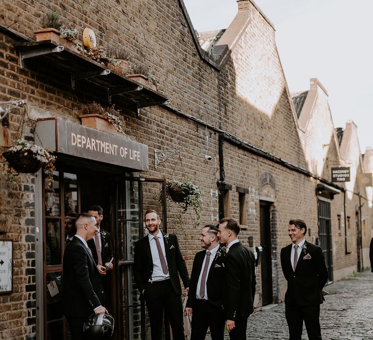 Groom gathers with his groomsmen outdoors as they wear black suits and white shirts 