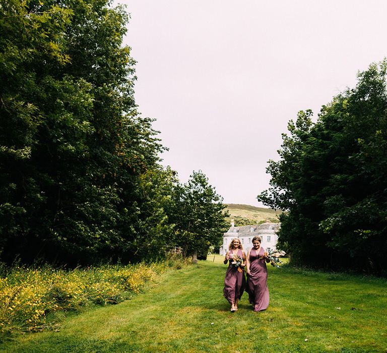 Bridesmaid in purple dresses walk along the fields together