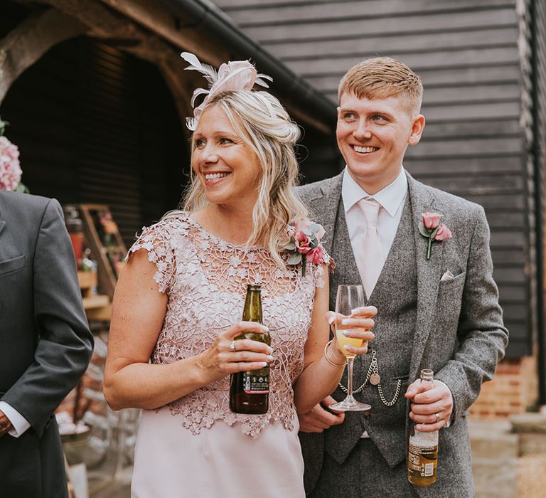 Groomsman in matching grey tweed suit with wedding guest in bliss pink dress and fascinator 