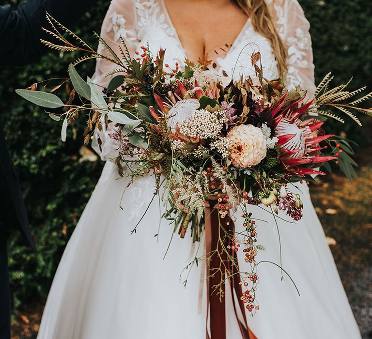 Autumn wedding bouquet tied with burgundy ribbon with green foliage, pink astilbe and king protea flowers 