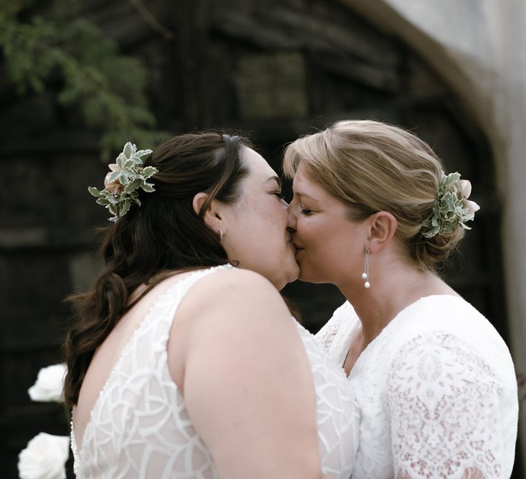 Brides in lace jumpsuits and diamanté belts share a kiss with dainty silver jewellery including pearls 