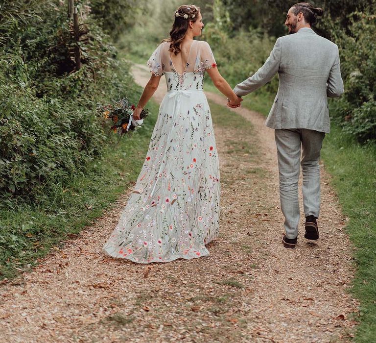 Bride in floral embroidered wedding dress holding hands with groom in grey suit