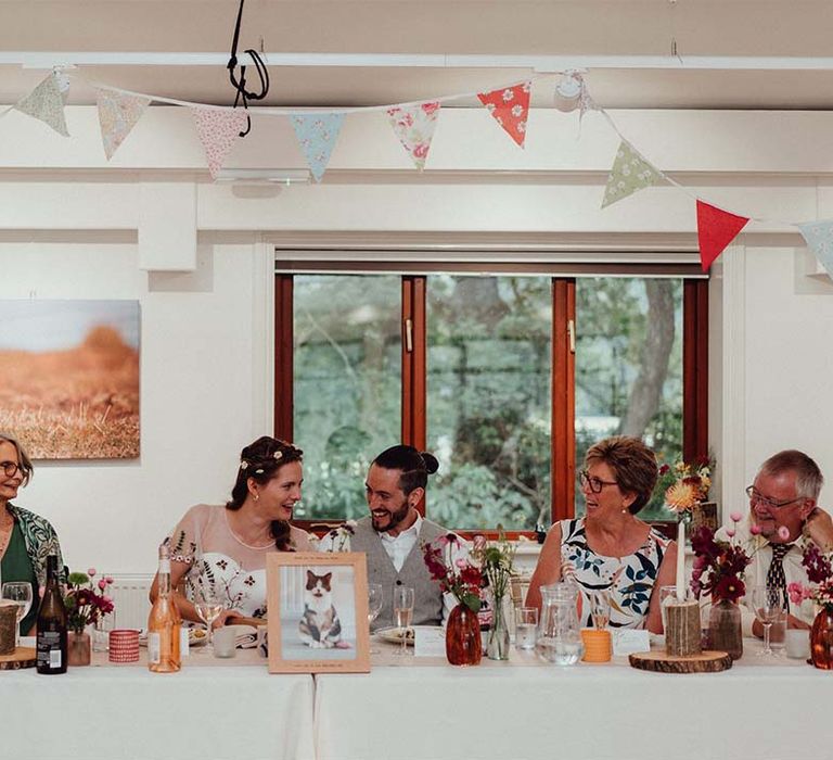 Top table with picture of their pet cat in wooden frame with tree trunk candle holders and floral bunting