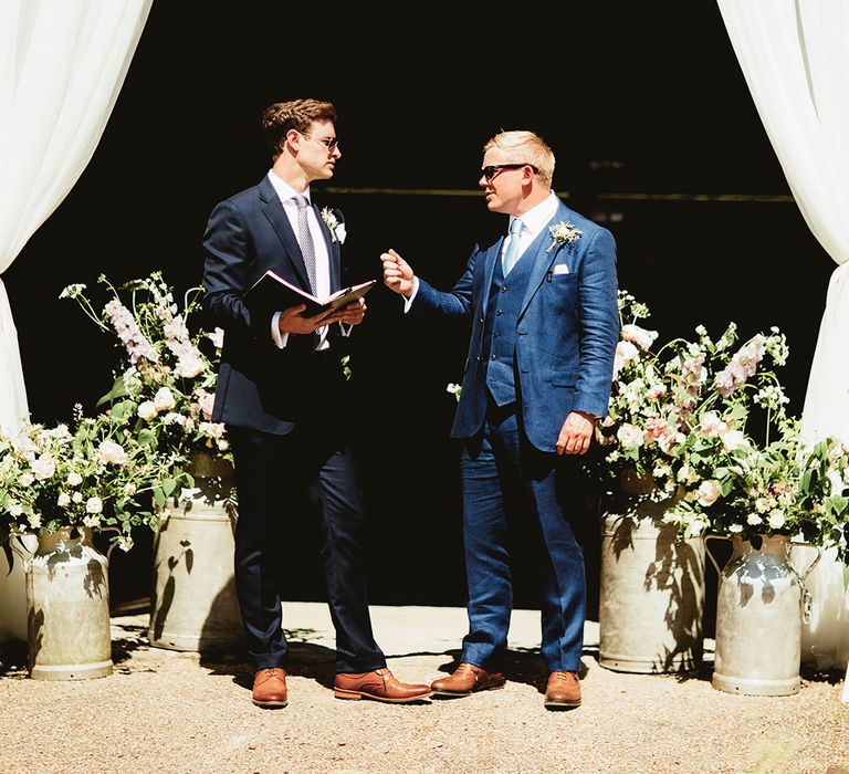 Groom in dark blue three piece suit with light blue tie speaks with the wedding celebrant 