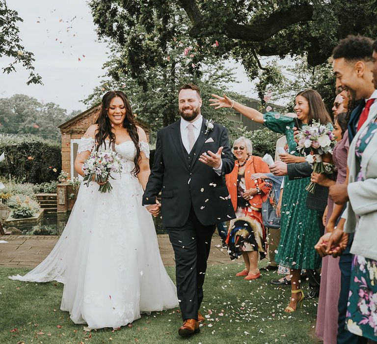 Bride and groom exit their wedding ceremony as husband and wife through pink confetti