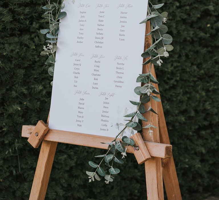 White seating chart on easel and decorated with foliage