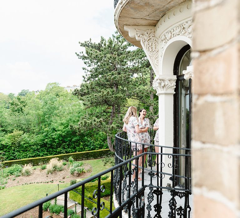 Bridesmaids in matching flower print pyjamas stand together on balcony of Pembroke Lodge