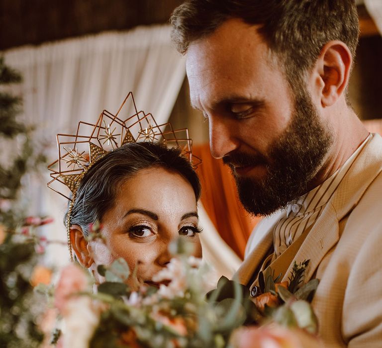 bride wearing a geometric celestial wire headband peeping over her wedding bouquet 