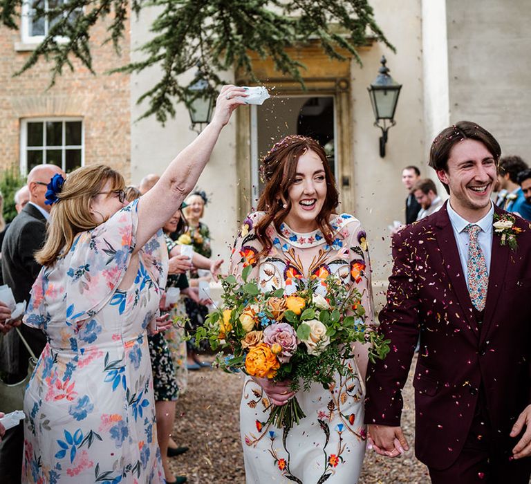 Bride and groom exit their ceremony to colourful confetti thrown by the wedding guests to celebrate 