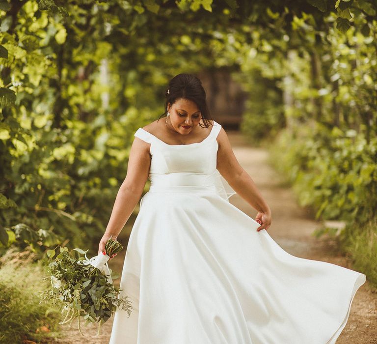 Bride walks along in her princess skirt bardot style wedding dress with classic white bouquet 