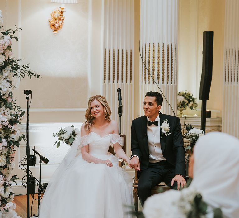 Bride and groom sit holding hands during their wedding ceremony 