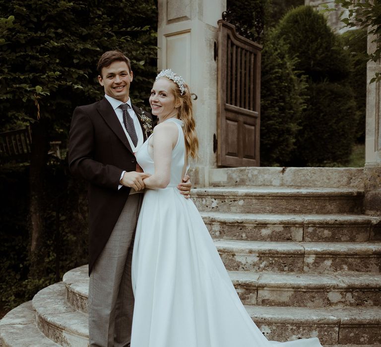 Bride smiles in pleated princess wedding dress with groom in morning suit after handfasting ceremony at Owlpen Manor 