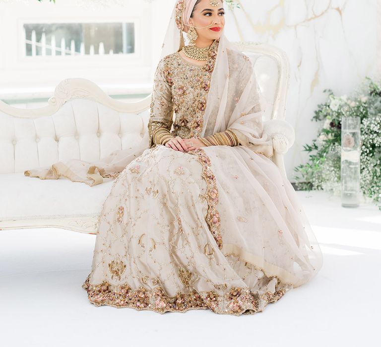 Bride sits on sofa as she wears traditional saree in gold and silver complete with colourful embellishment for Walima ceremony 