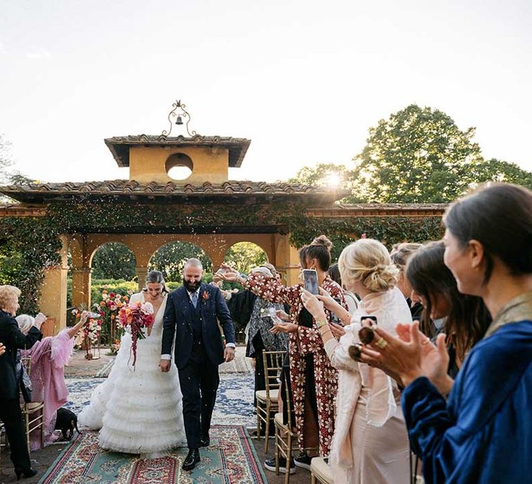 Bride & groom walk through wedding guests who throw confetti around them outdoors on their wedding day